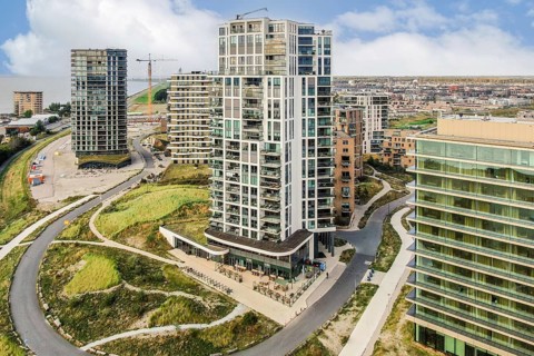 A scenic view of a contemporary apartment building surrounded by greenery and a bustling city