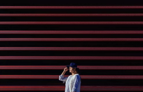 A fashionable woman in a blue hat stands confidently against a striking background of horizontal
