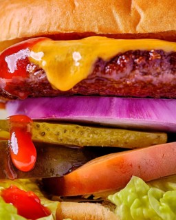 A stacked cheeseburger featuring a beef patty, melted cheese, pickles, tomato, lettuce, red onion