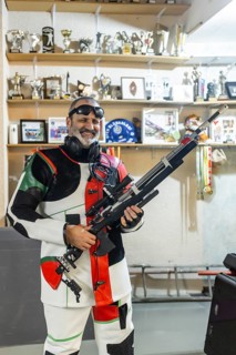 A blind shooter in action, wearing a specialized suit and holding a rifle, standing in front of a