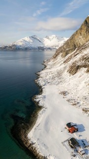 A stunning aerial view of a snow-covered Nordic coastline, showcasing majestic mountains and the