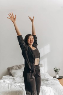 A smiling woman stretches energetically in a sunlit room, embodying morning vitality and healthy