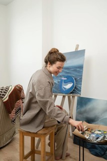 A female artist joyfully paints a whale on a canvas in a cozy home studio. Surrounded by her tools