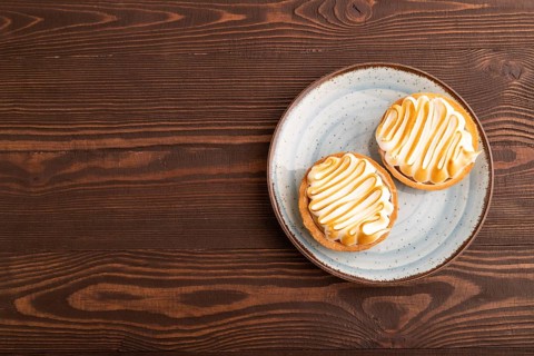 French lemon tart with meringue on brown wooden background, top view, flat lay, copy space
