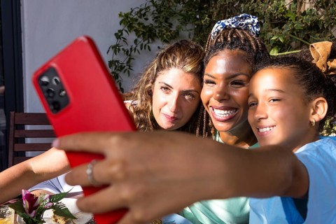 Joyful moment of a lesbian couple with their child, capturing a selfie outdoors. Embracing