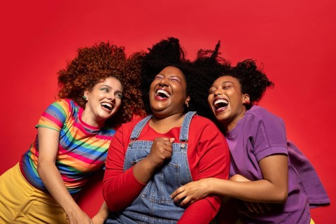Three friends share a moment of pure joy and laughter, lying on a vibrant red background. Their