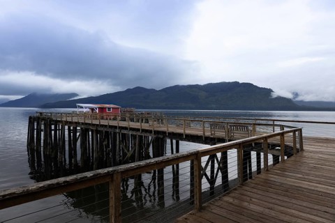 A serene landscape featuring a wooden pier extending into calm waters in Hoonah, Alaska, with a