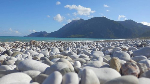 Pebble beach with mountains in the background under blue sky and calm atmosphere, hiking on the