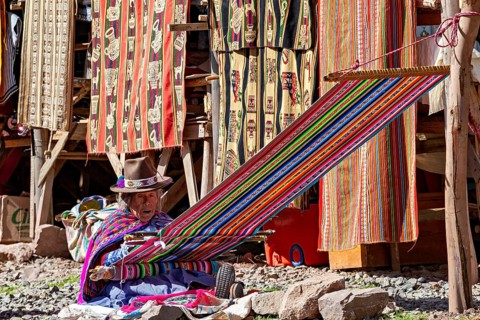 Man in traditional clothing weaves colorful fabric in a craft stand, elderly traditionally dressed