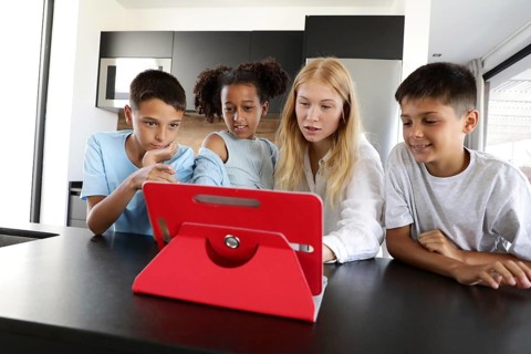 Three children and a young woman gather around a red tablet, engaged in a fun and educational