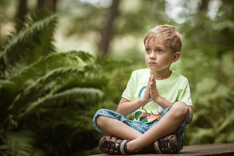 5-6 years old boy meditates on the bench in the park