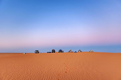 Vehicles and tents standing on a sand dune under an open sky at sunrise, camping in the sand dunes
