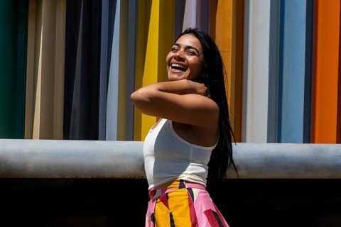 A joyful woman in a vibrant outfit stands against a backdrop of modern architecture, creating a