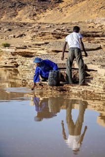 Two people drawing water from a spring in a barren desert landscape, Tuareg fetching water in the
