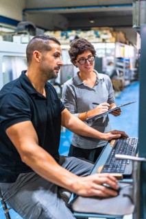 Vertical photo of a male engineer showing computer screen data to female manager at factory