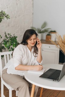 A nutritionist in a home office setting consults with a client over the phone. She takes notes on a