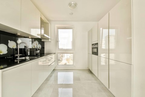 A bright modern kitchen featuring sleek white cabinets, glossy countertops, and a window with a