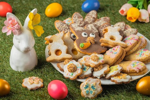 Different Easter cookies on a plate next to a porcelain hare, Easter eggs and flowers in the grass