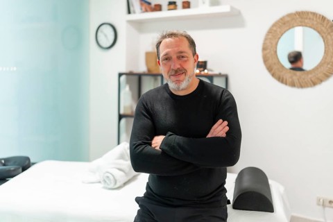 Male professional masseuse standing with arms crossed, confidently smiling at the camera in a