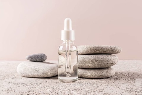 A minimalist serum bottle with a dropper rests on smooth, stacked stones on a natural textured