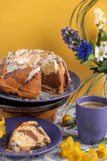 Cut marble bundt cake, cake on blue plates with icing, surrounded by flowers and a cup of coffee,
