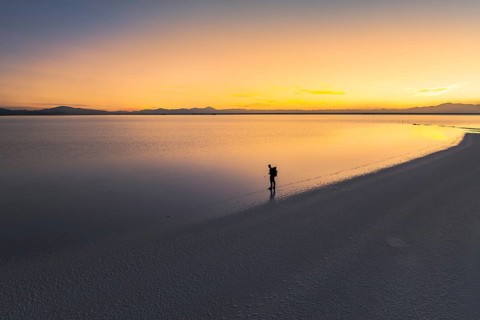 A lone traveler stands at the edge of a vast salt flat in Salinas Grandes, Salta, Argentina, as the