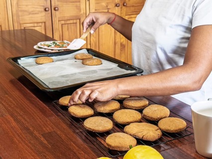 A woman bakes fresh cookies on a wooden table. The scene shows cookies placed on a cooling rack