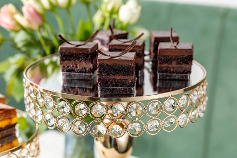 Luxurious chocolate cake bites on a decorated mirrored stand with a floral background. Perfect for
