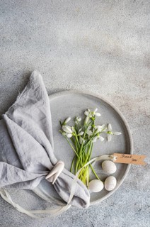 Top view of a serene still life featuring snowdrops in a tray with Easter eggs and a linen napkin.
