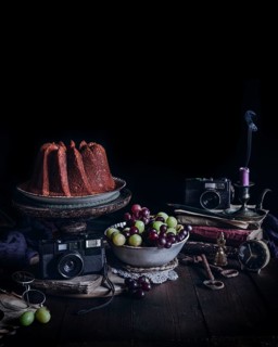 A captivating vintage still life featuring a cake on a stand, surrounded by antique cameras, a bowl