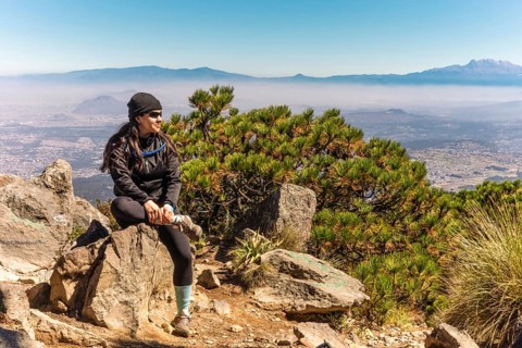 A woman sits on a rock, soaking in the stunning mountain landscape under a clear blue sky Perfect