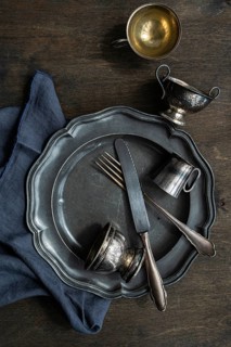 A rustic arrangement of vintage metal tableware, featuring a plate, fork, knife, and two small cups