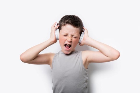 A young boy in a gray tank top passionately listens to music on white headphones, eyes closed,