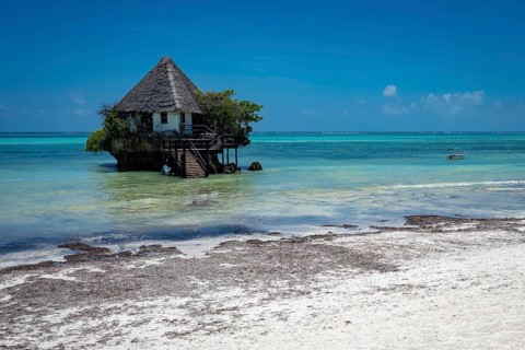 Building built on a coral outcrop in turquoise ocean water, with a small boat arriving at the