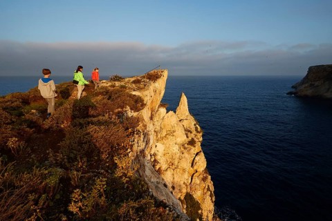 Three people explore a cliff overlooking the sea at sunrise, morning light, Tsichli Babas islet,