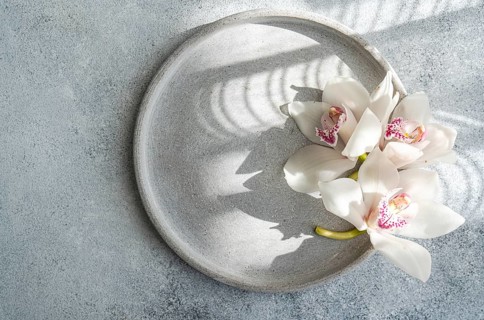 Beautiful white orchids arranged on a round grey ceramic plate create an elegant and minimalist