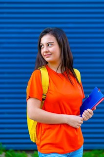 Vertical photo of a cute student with casual colorful clothes and textbooks standing outdoors