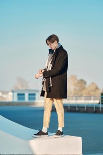 Young man in old wool coat, scarf and short trousers standing in profile outdoor