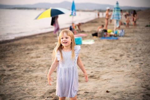 A cheerful young girl plays on a sandy beach in Italy, smiling as she enjoys the warm summer breeze