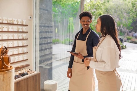 Two store employees in aprons engage in a conversation about product display in a stylish, sunlit
