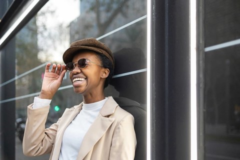 A stylish black woman wearing sunglasses and a hat enjoys a moment in the city Her fashion and