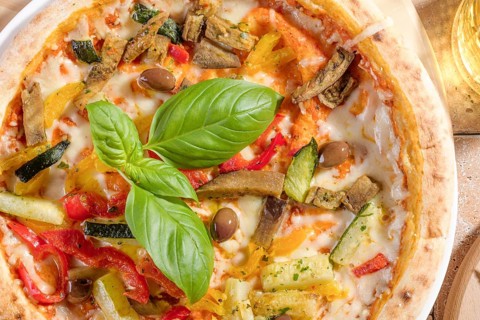 A delicious vegetarian pizza topped with fresh basil, zucchini, eggplant, and olives, baked to
