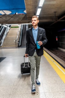 Businessman walking through a bustling subway station, carrying luggage and sipping coffee,