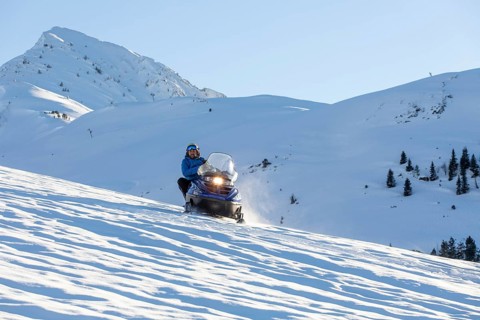 A person rides a snowmobile across a vast, snow-covered landscape in the winter mountains,