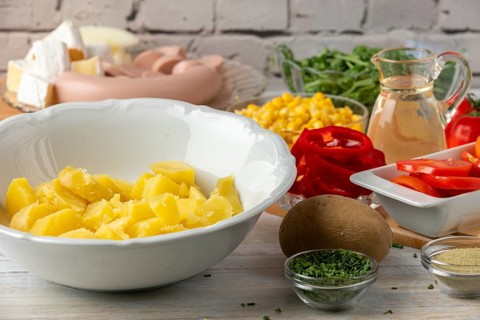 Potatoes in a bowl surrounded by other ingredients such as peppers, corn, sausage and arugula
