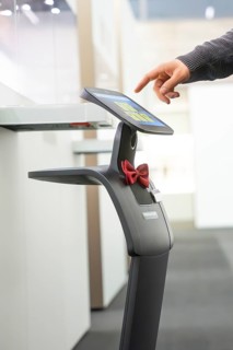 A robot-like device with a red ribbon is touched by a hand on the screen, interactive guided tours
