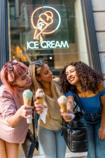 Vertical photo of three female friends showing at camera delicious ice cream cones outdoors