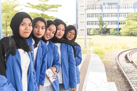 A group of Asian students in hijabs smile joyfully as they return to their campus, wearing blue