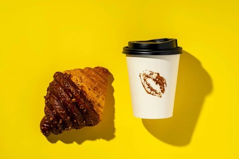 Top view of a decadent chocolate croissant paired with a take-out coffee cup, which features a
