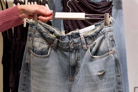 A distressed denim jeans is displayed on a hanger, showcasing its frayed waistband and vintage look